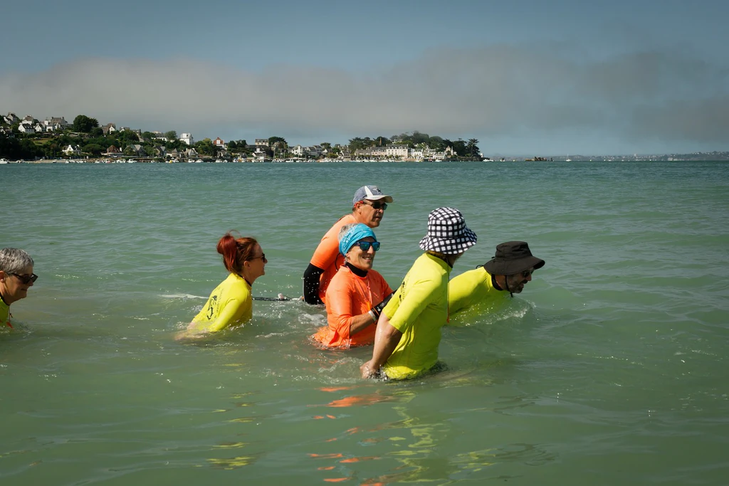 Cinq pratiquants de longe-côte entrent dans l'eau et se mettent en position pour démarrer leur session